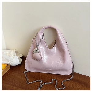 Detail view of pink glossy pleated handbag with heart charm and thin metal chain strap