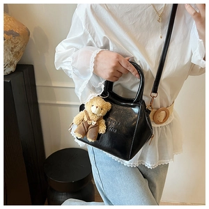 Detail of black glossy crossbody bag with embossed text and a cute teddy bear charm