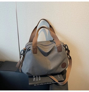 Close-up of gray travel bag on leather sofa with adjustable strap and leather logo