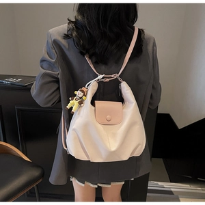 Detail of a pleated cream pink canvas tote with doll pendant and color-block flap design