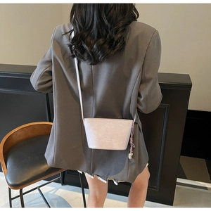 Détail du sac seau en cuir violet clair avec breloque métallique sur un blazer gris