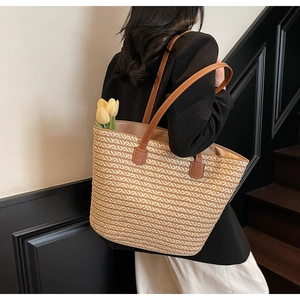 Detail of hand-woven straw tote bag with brown leather straps shown in a chic urban setting