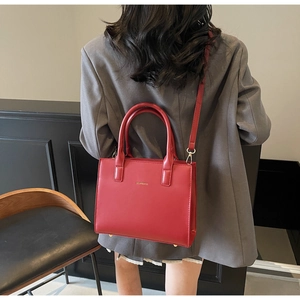 Red leather tote bag on grey suit featuring double handles and adjustable strap