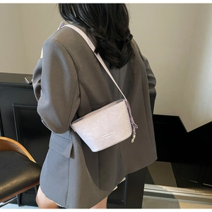 Détail du sac seau lilas avec texture plissée et breloque dorée sur un blazer gris