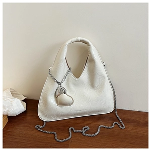 Detail of creamy white dumpling bag with heart charm and silver chain on wooden stand