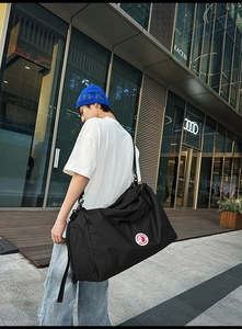 Black high-density nylon tote bag shown in use with adjustable strap and brand logo