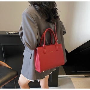 Detailed view of a red matte leather crossbody bag worn by a model in a grey suit
