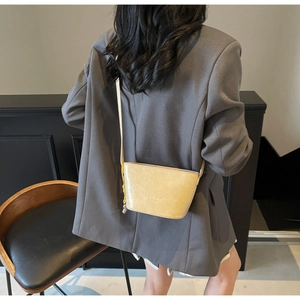 Détail d'un sac seau crème à texture froissée brillante porté sur un blazer gris