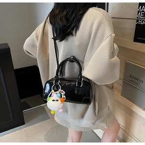 Detail view of black patent leather bowling bag with detachable strap and plush pompom charm