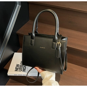 Close-up of black leather trapezoid handbag with gold logo on dark wood stairs
