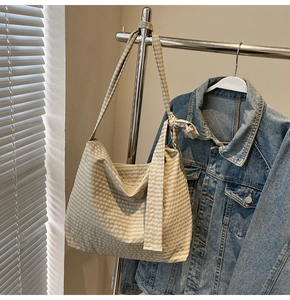 Detail of beige check canvas hobo bag with decorative bow hanging on a metal rack