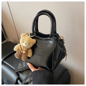 Detail of black patent leather handbag with embossed letters and a cute teddy bear charm