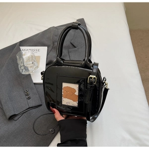 Detail of black patent leather crossbody bag with a cartoon teddy card on a bed