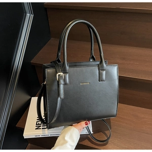Detail of a structured black leather tote bag with gold logo and adjustable shoulder strap