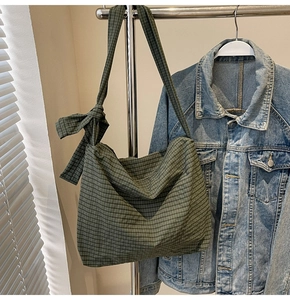 Detail of dark green checkered tote bag featuring a decorative ribbon bow on the shoulder strap