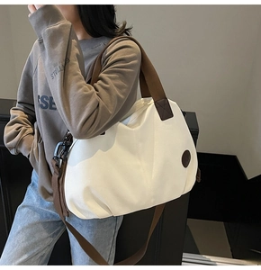 Detail of a large white canvas travel bag with wide brown shoulder straps on a model