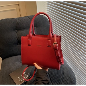 Red matte leather tote bag detail with gold logo displayed on a blue velvet chair