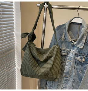 Close-up of green checkered tote bag with decorative bow hanging on a metal rack