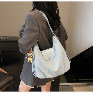 Detail view of light blue canvas tote bag on model's shoulder with cute doll pendant