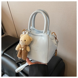 Detail of light blue textured leather tote with embossed lettering and plush bear charm