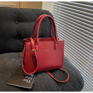 Detail of red leather crossbody tote bag with gold brand lettering on dark sofa