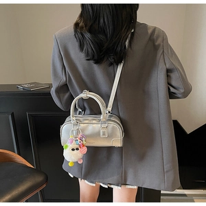 Silver metallic bowling handbag with plush bear charm styled on a blazer sleeve