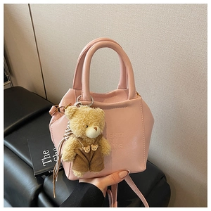 Detail of light pink shoulder bag with teddy bear pendant on a leather surface
