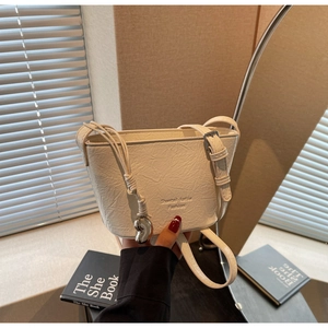 Détail du sac seau crème avec texture plissée et pendentif en forme de cœur argenté
