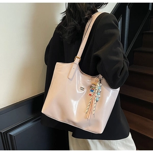 Close-up of pink patent leather tote bag with metallic logo and decorative tassel charm