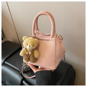 Detail shot of a pink leather crossbody bag with a plush bear charm and adjustable strap