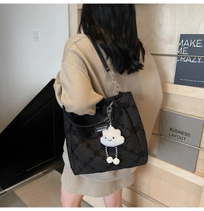 Detail of black quilted tote bag with white cloud plush charm and long leather straps