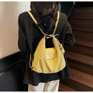 Detail of bright yellow waterproof nylon convertible backpack on a model with charm