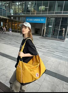Close-up of a large yellow nylon tote bag with black straps in an outdoor urban setting