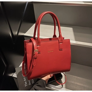 Detail of red leather handbag with gold logo, double handles and adjustable strap