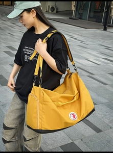 Outdoor shot of a large yellow nylon tote bag with black bottom and side zip compartment