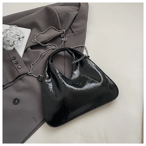 Detail of black glossy pleated dumpling bag with silver chain strap on a blazer