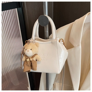 Close-up of cream PU leather handbag with a plush bear charm and embossed logo