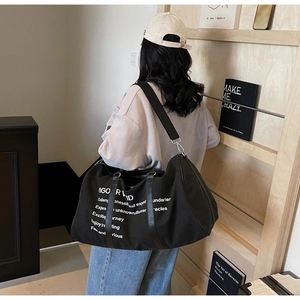 Close-up of a black canvas travel tote bag with white inspirational text on the strap