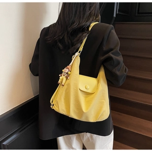Detail of bright yellow hobo bag with a decorative cartoon charm and front flap pocket