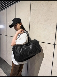 Detail of black faux leather travel bag with embossed houndstooth texture and metal hardware