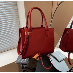 Close-up of red leather tote bag with gold brand logo and adjustable shoulder strap