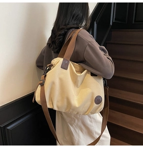 Detail of a large beige canvas tote bag with brown straps and brand leather patch