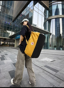 Outdoor shot of a large yellow and black nylon tote bag with handles and wide shoulder strap