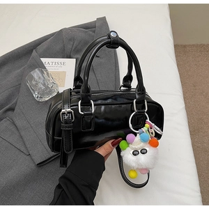 Detail of black patent leather bowling bag with a white furry monster charm and silver hardware
