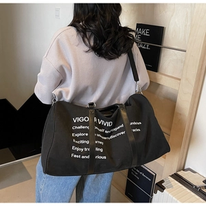 Close-up of black canvas travel bag with white artistic letters worn by a model