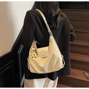 Detail of a beige canvas tote bag featuring pearl charms and a cartoon pendant on the strap