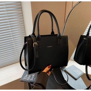 Close-up of a black minimalist leather handbag with silver lettering and top handles