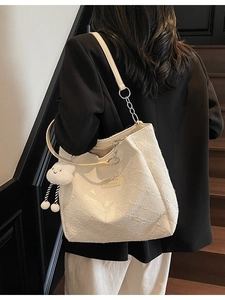 White textured tote bag with metal chain strap and plush cloud charm on a model
