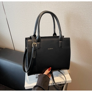 Detail of a black leather handbag with a gold logo and an adjustable shoulder strap