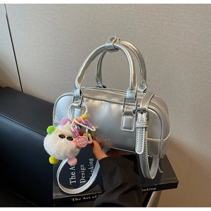 Detailed view of silver bowling bag with plush charm on a modern black leather sofa